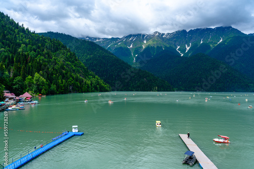Alpine Lake Ritsa. Tourists on catamaran sailing along lake among mountains.