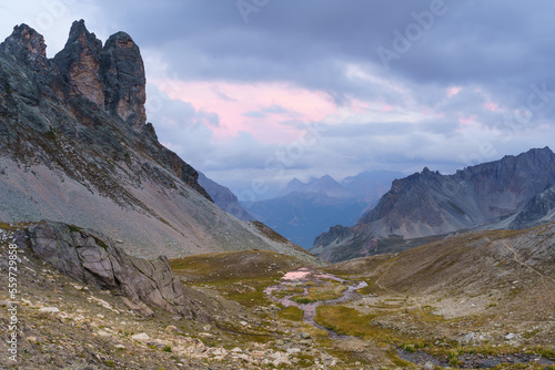 A scenic view of a mountain valley with grey clouds in Névache, France. This image captures the beauty and tranquility of nature in the Hautes-Alpes region.
