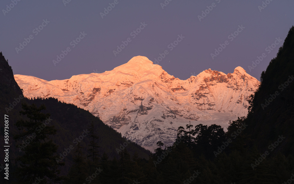 A stunning view of Manaslu peak in Nepal, the eighth highest mountain in the world, at sunset. The orange glow of the sun reflects on the snow-capped summit.