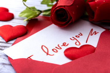 Note that says "I love you" inside an envelope with hearts and roses on wooden table