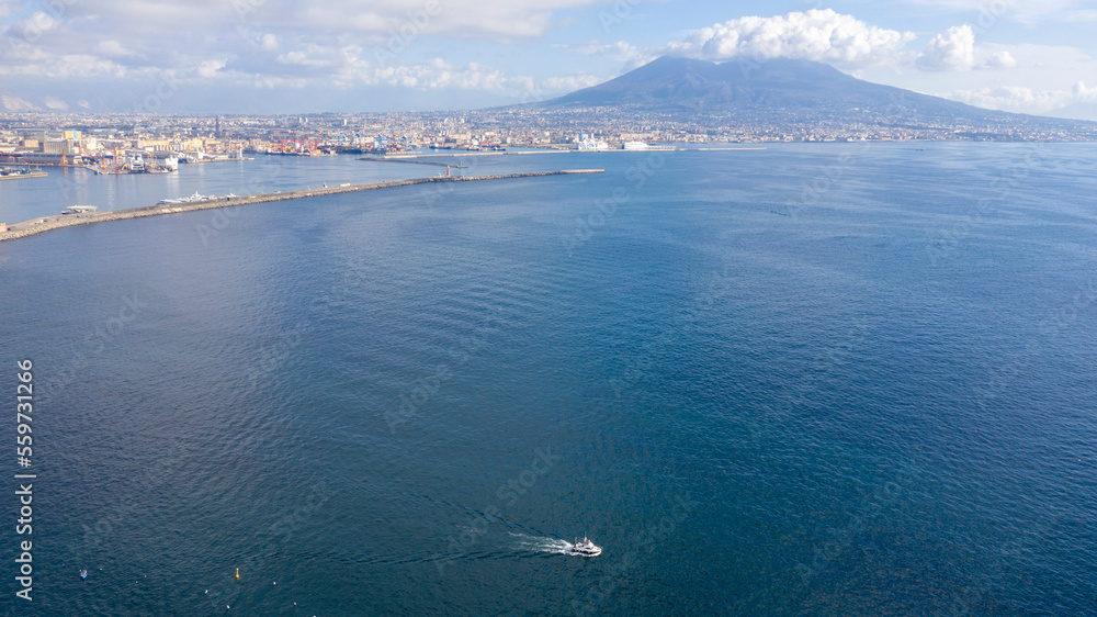 Aerial view of the port of Naples, Italy. In the background the Vesuvius volcano which dominates the panorama. A small boat crosses the gulf.