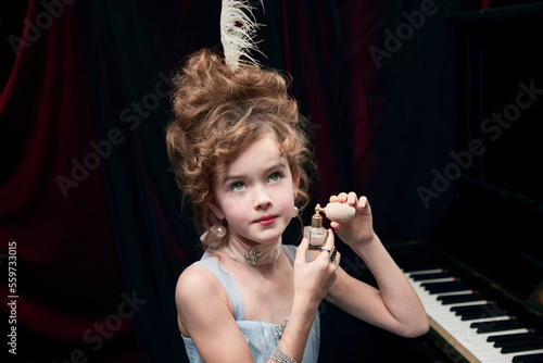 Portrait of beautifl little girl, child in image of medieval royal person with amazing hairstyle applying face powder photo