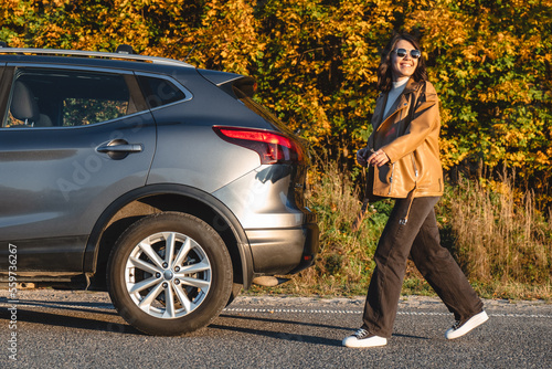 On an autumn forest background, a smiling woman walks in front of her car