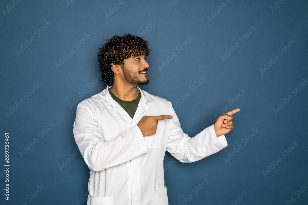 Portrait of smiling male doctor with clipboard standing isolated on blue background. Pointing smth. Portrait of smiling male doctor with clipboard standing isolated on blue background. Pointing smth.