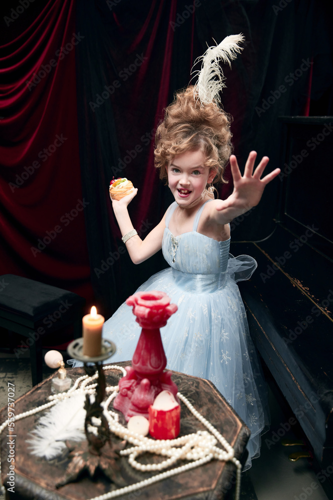 Portrait of little girl, child in image of medieval royal person playing with cake. Delicious food