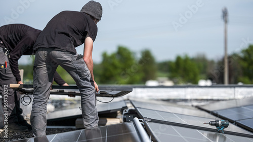 Male team engineers installing stand-alone solar photovoltaic panel system. Electricians mounting blue solar module on roof of company roof. Alternative energy concept
