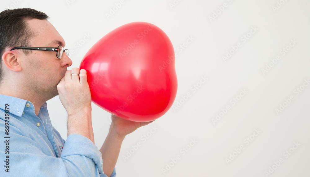 Side view on a man blowing heart balloon preparing for valentines day or anniversary Side view on a man blowing heart balloon preparing for valentines day or anniversary