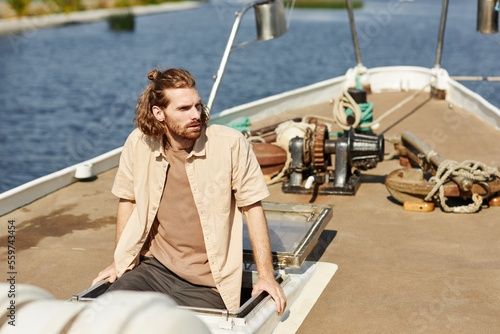 Portrait of bearded young man sailing on boat and looking away lit by sunlight, copy space