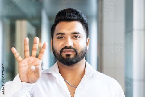 Happy smiling young south asian Indian man pointing up 4 fingers, showing number four, forth place or 4 points gesture