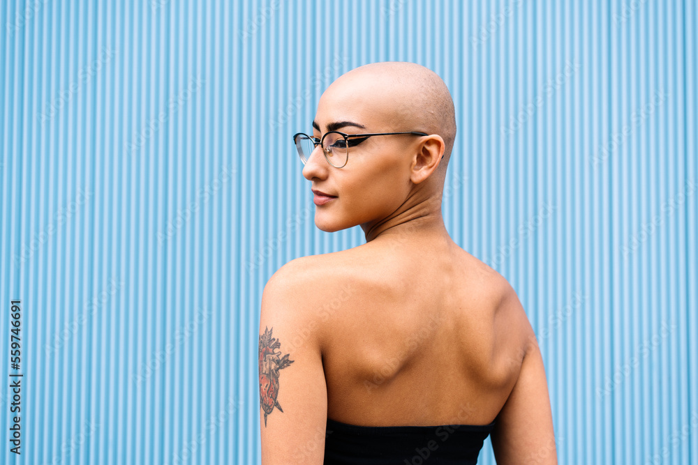 Woman with shaved head in front of blue wall Woman with shaved head in front of blue wall