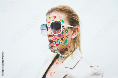 Woman with multi colored stickers on face and necklace in mouth against white background photo