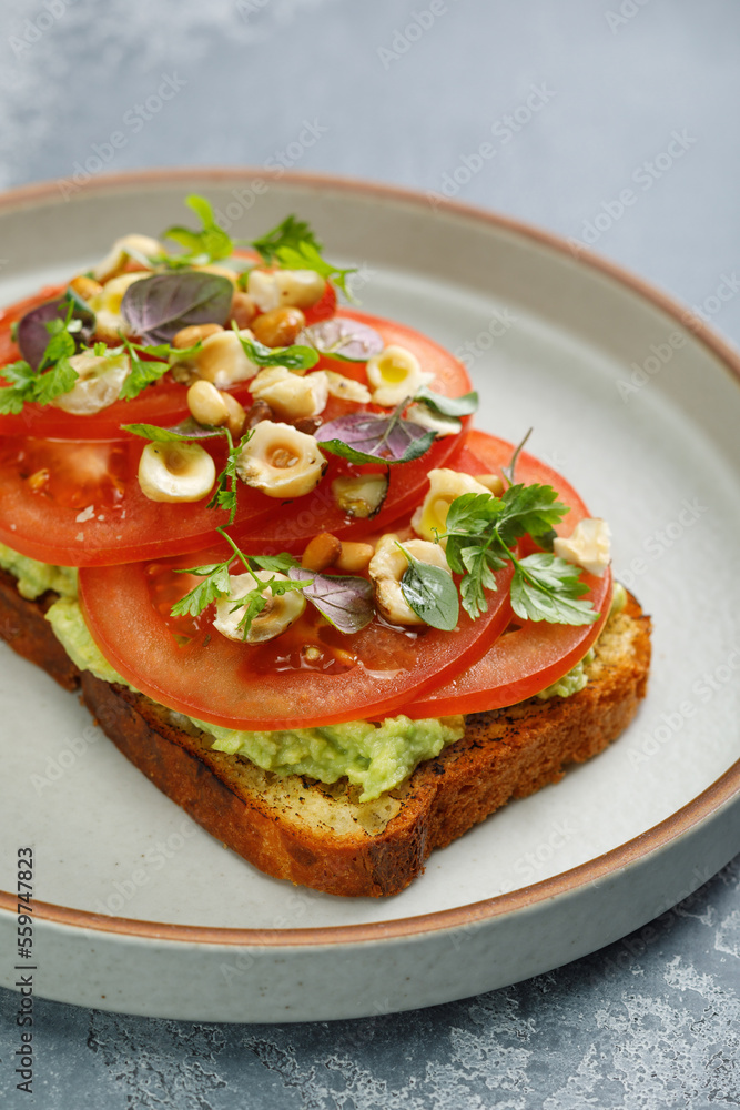 Toast with guacamole and slices of fresh tomatoes with fried hazelnuts on top. Vegetarian cuisine