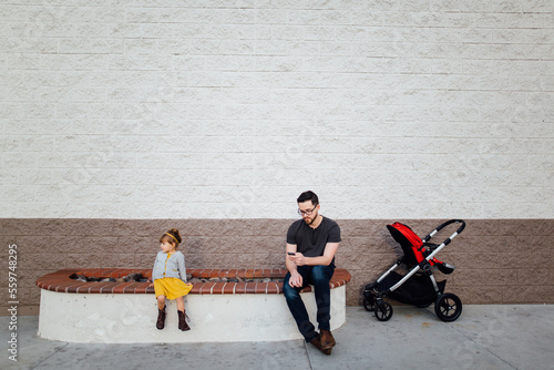 Father checking phone while sitting outside a building with children photo