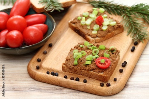 Pate spread from deer meat on whole grain bread and green onion. Sandwich with meat pate on cutting board, fresh tomatoes and spices for venison around. Decorated with spruce branch.