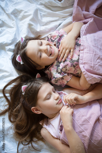Two sisters girls lie under pink blanket. Sisters' girls rest peacefully together.
