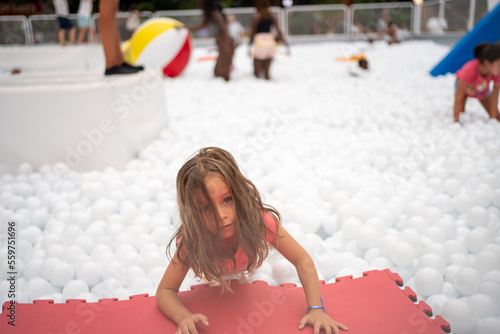 Happy little girl playing white plastic balls pool in amusement park. photo