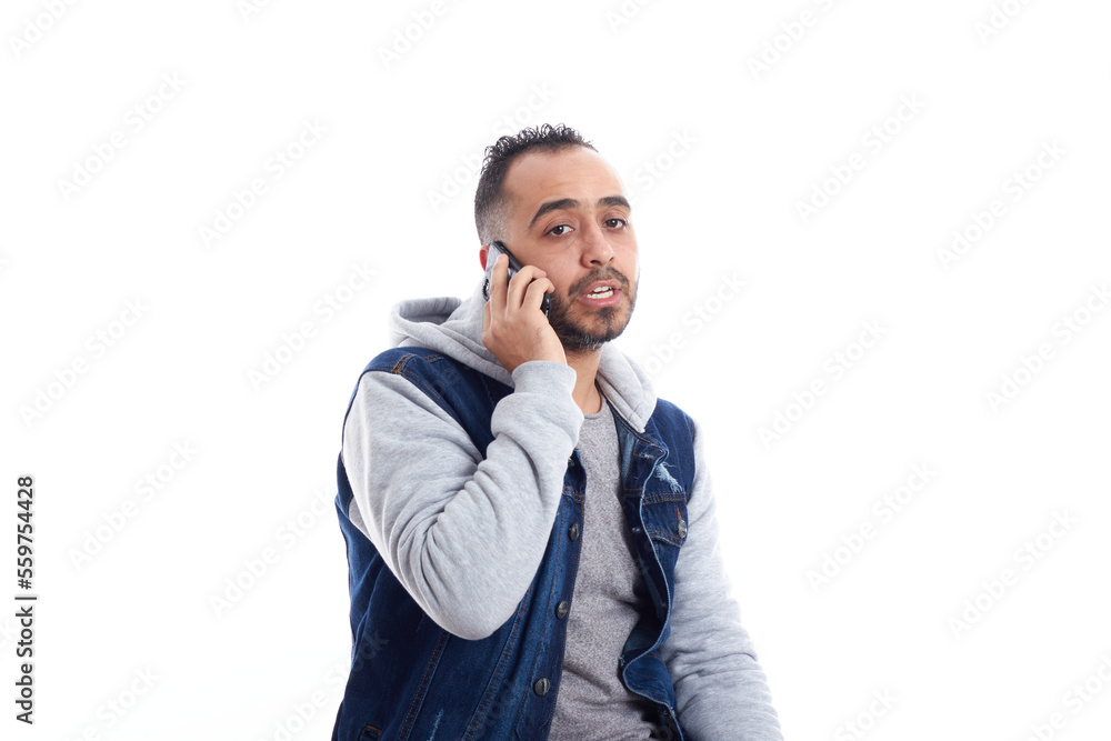Isolated portrait of a cheerful Egyptian businessman wearing a blue shirt, jeans and watch and talking on his smartphone sitting on a chair. Isolated portrait of a cheerful Egyptian businessman wearing a blue shirt, jeans and watch and talking on his smartphone sitting on a chair.