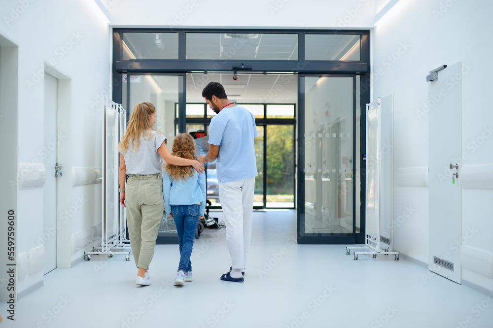 Rear view of young multiracial doctor talking with mother and little girl at hospital corridor,showing them x-ray image. Rear view of young multiracial doctor talking with mother and little girl at hospital corridor,showing them x-ray image.
