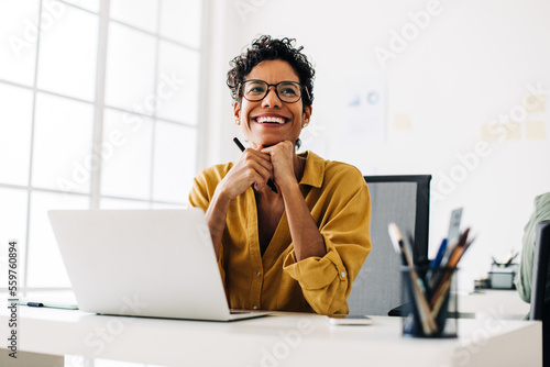 Happy graphics designer sitting at her desk thinking about a design photo