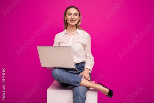 Young woman in a white shirt making a video call from a laptop on a pink background