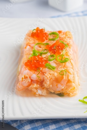 Fish aspic of shrimp, salmon and boiled quail eggs garnished with red caviar and green onions on a white plate on a light background. Recipes fish and seafood. photo