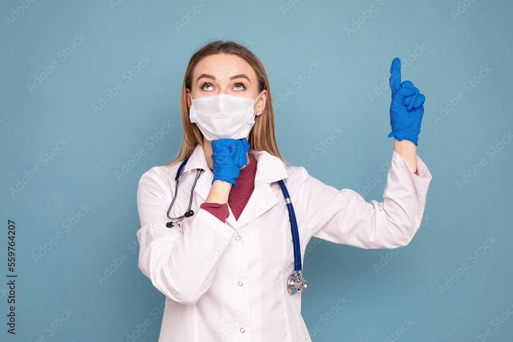 Portrait of a female doctor in a white coat and a medical mask. Emotional portrait on a blue isolated background Portrait of a female doctor in a white coat and a medical mask. Emotional portrait on a blue isolated background