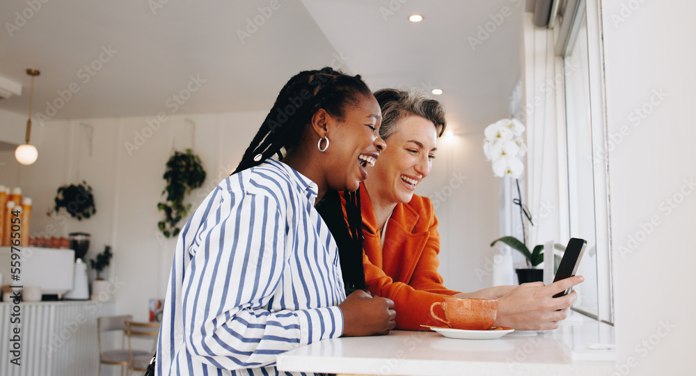 Smiling business women video calling their colleagues on a smartphone in a cafe Smiling business women video calling their colleagues on a smartphone in a cafe