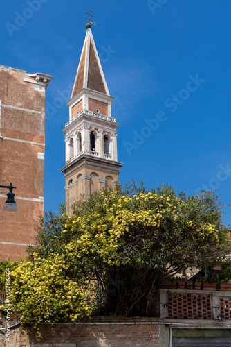 Bell tower of San Francesco della Vigna church in Italy. Narrow streets of Venice and beautiful blooming spring plants and clear blue sky.