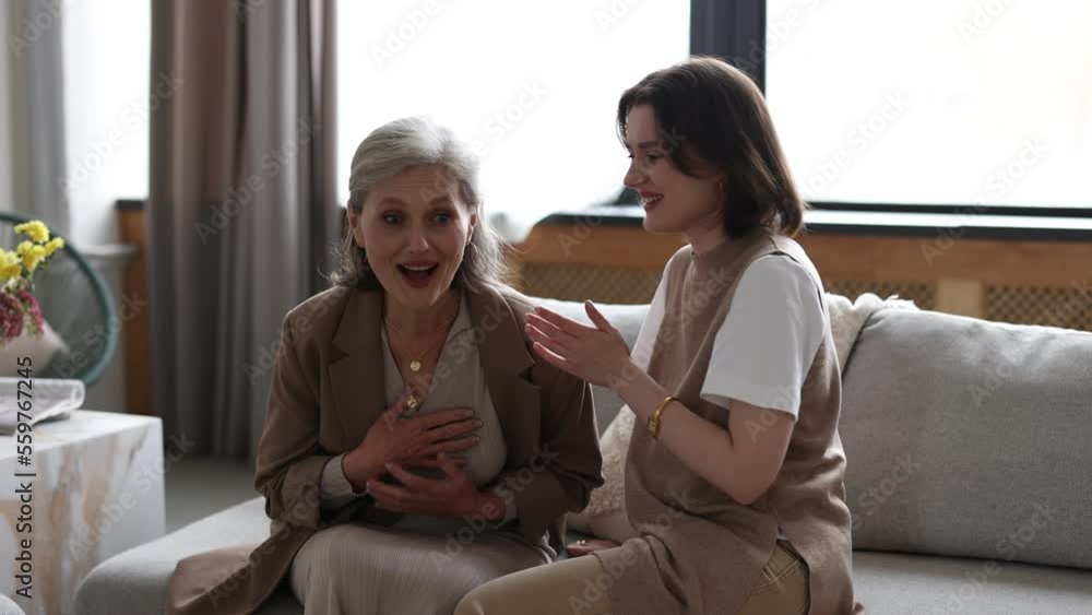 adult daughter tells the news to her mother in a cozy environment whispering in her ear adult daughter tells the news to her mother in a cozy environment whispering in her ear