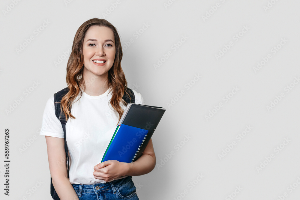female student with backpack smiles and holds a notebook, copybook, folder in the hands isolated on dark white background female student with backpack smiles and holds a notebook, copybook, folder in the hands isolated on dark white background