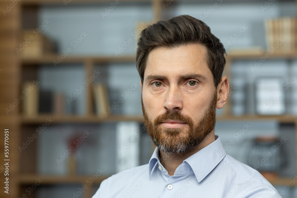 Close up photo of serious boss in shirt in home office, mature man with beard looking at camera thinking, businessman investor headshot. Close up photo of serious boss in shirt in home office, mature man with beard looking at camera thinking, businessman investor headshot.