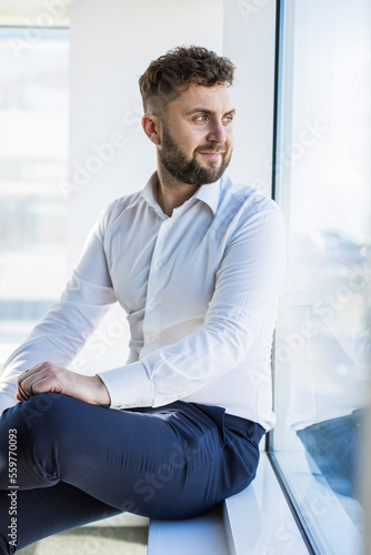Portrait of a business young successful man in a modern office sitting by the window against the backdrop of the city