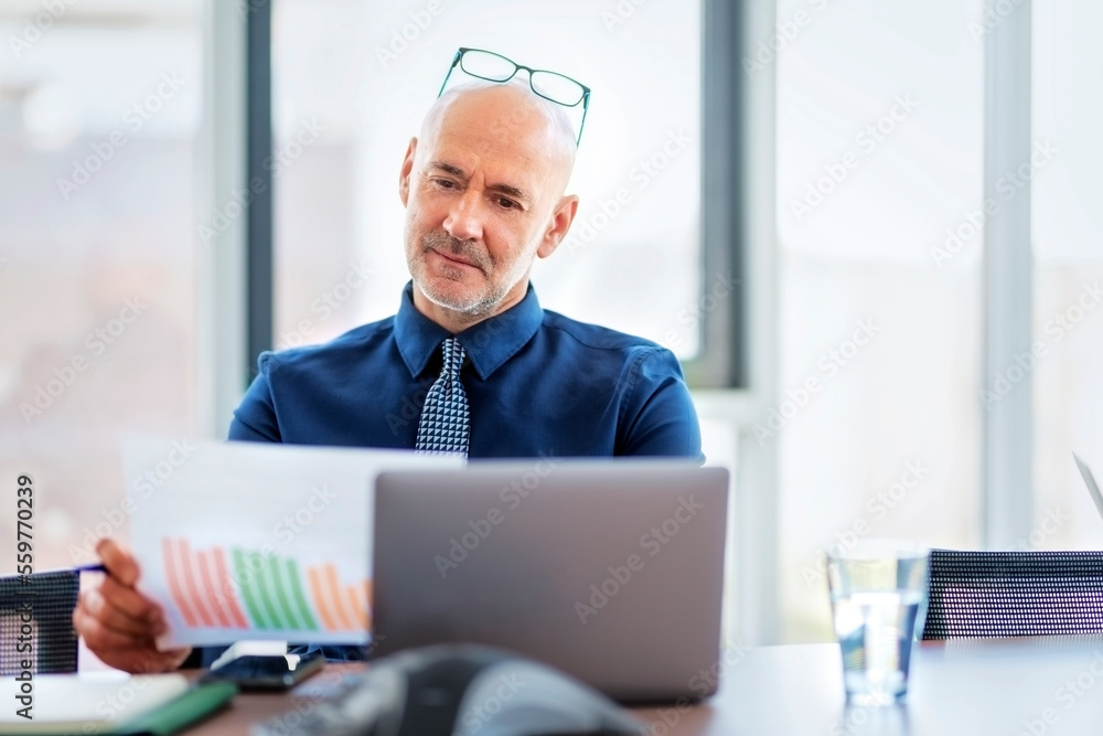 Middle aged businessman usin laptop and having video conference while working at the office