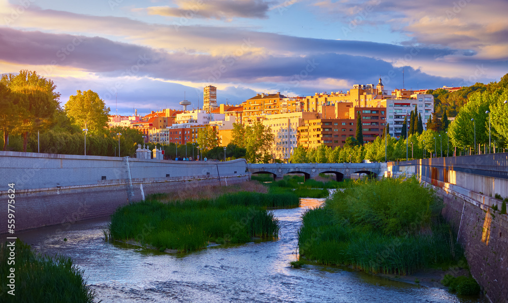 Madrid, Spain. Panoramic view at river Manzanares and houses of residential district during sunset with picturesque sky clouds. Embankment green trees