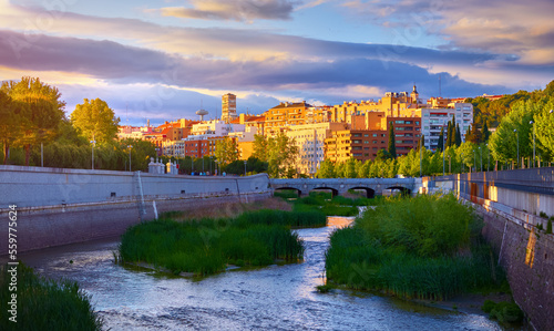Madrid, Spain. Panoramic view at river Manzanares and houses of residential district during sunset with picturesque sky clouds. Embankment green trees