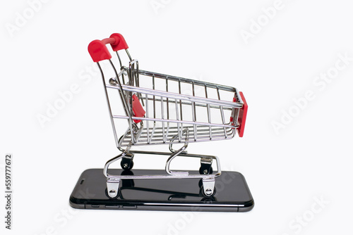 A small shopping cart stands on a mobile phone on a white background. The concept of online shopping using the phone. Convenience of remote purchases using modern technologies in the form of a phone © halcon1