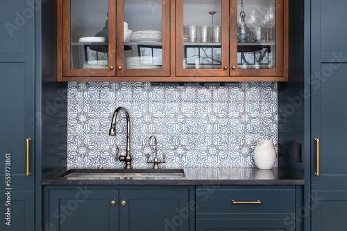 Foto A kitchen sink with a beautiful pattern tiled backsplash with a chrome faucet, black granite countertops, and surrounded by blue and wood cabinets