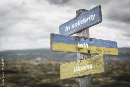 in solidarity with ukraine text on wooden signpost with the ukranian flag painted on it. Peace and war concept.