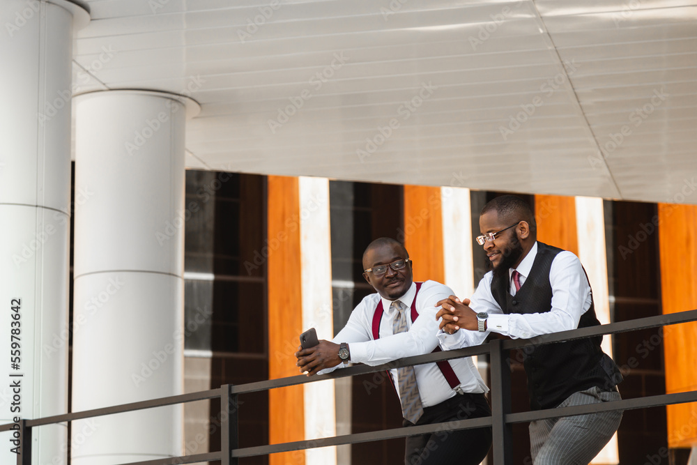 Portrait of two dark-skinned businessmen talking in the background of a modern building exterior. Friendly meeting outdoors