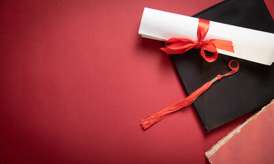 Graduation hat and diploma on the bordeaux background.