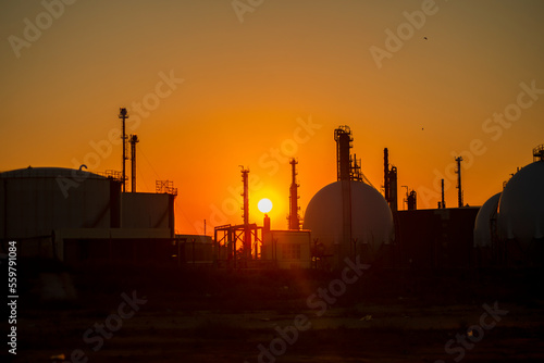 silhouettes of structures, pipes, oil storage tanks, pipelines of a petrochemical plant in the backlight of the sun at sunset and a sun disk.