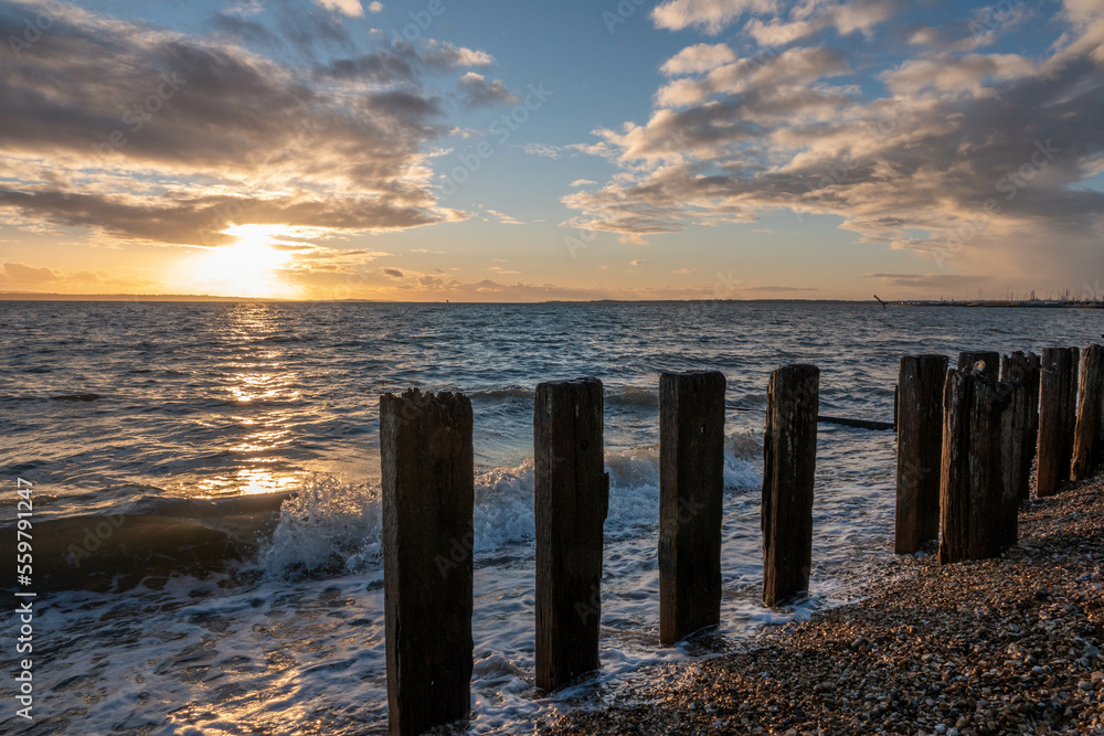 bright orange sunset over the waves and groynes in the sea on a deserted beach