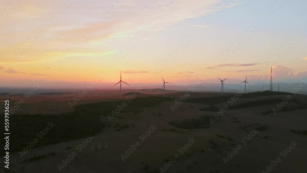 Aerial small wind turbines in field with bright orange sunset blue sky wind park slow motion drone turn. Silhouettes windmills, large orange blue sunset sky. Alternative energy concept Aerial small wind turbines in field with bright orange sunset blue sky wind park slow motion drone turn. Silhouettes windmills, large orange blue sunset sky. Alternative energy concept