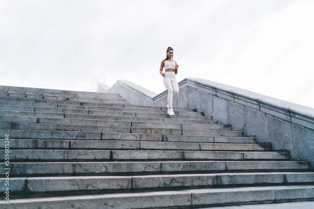Slim Hispanic sportswoman running downstairs during training on street