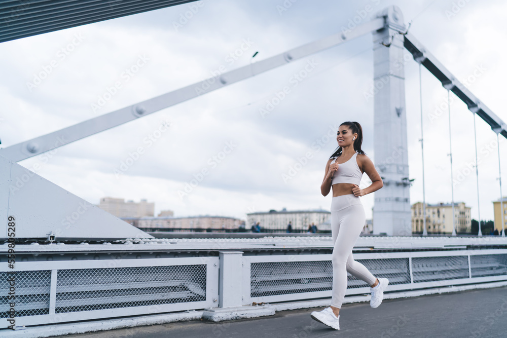 Motivated Hispanic female athlete running on bridge and smiling Motivated Hispanic female athlete running on bridge and smiling