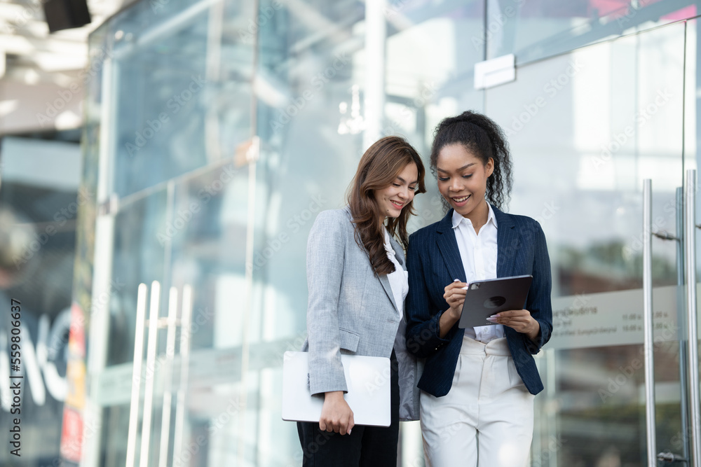 Two Asian businesswomen discussing business information while standing outside the office. Two Asian businesswomen discussing business information while standing outside the office.