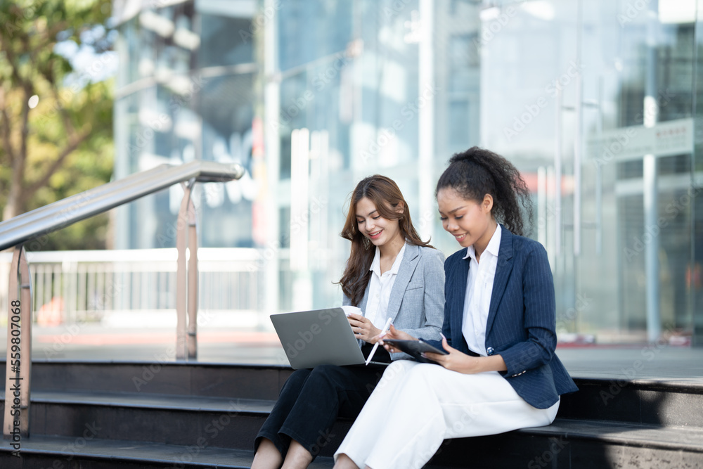 Two Asian businesswomen discussing business information while standing outside the office. Two Asian businesswomen discussing business information while standing outside the office.