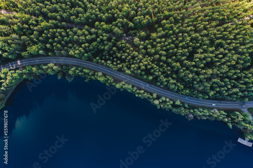 Aerial view of road with green woods by blue lakes water in Finland.
