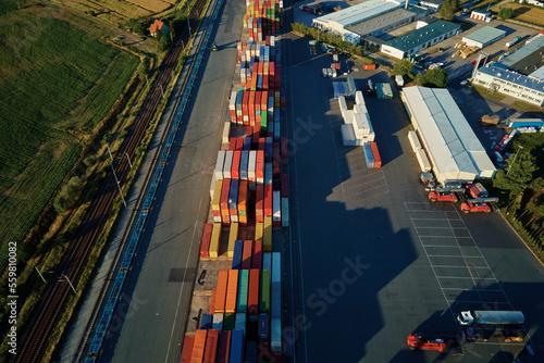 Shipping containers in terminal, Unloading containers in warehouse on railroad platform with cranes and forklifts, aerial view