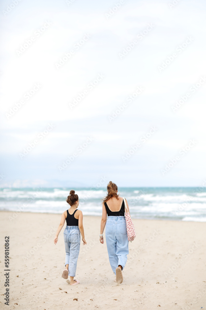 Happy family on beach vacation. Back view of mother and little daughter are walking together and holding hands on beach. Mom and child girl kid enjoy and having fun at summer holidays